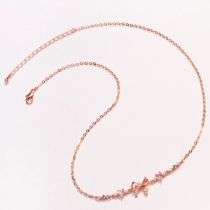 Detail of rose gold bow pendant necklace inlaid with pink and purple cubic zirconia