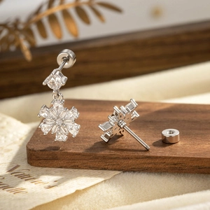 Elegant silver snowflake stud earrings with sparkling cubic zirconia on a rustic wooden stand
