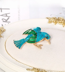Close-up of elegant gold-plated bird brooch with blue and green enamel textures