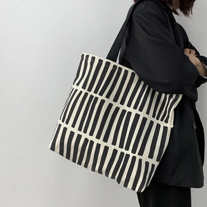 Detail of minimalist black and white striped canvas tote bag worn by a side-view model