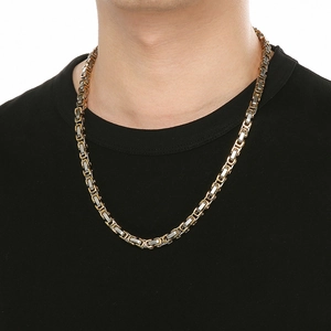 Close-up of a thick two-tone Byzantine chain necklace worn by a male model on black shirt