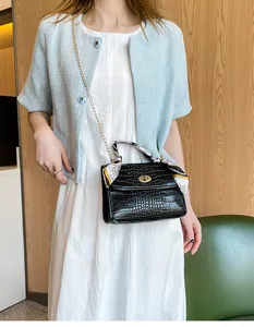 Detail of black crocodile texture handbag with decorative silk scarf and gold chain strap