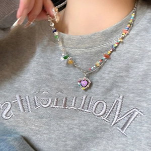 Detail of layered necklace with colorful beads and purple heart pendant on grey hoodie