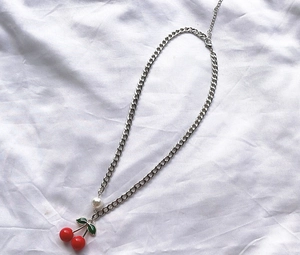 Detail of silver Cuban chain necklace with red cherry pendant and a pearl accent