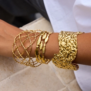 Detail of stacked gold hollow mesh, fish motifs, and hammered wide open cuff bracelets