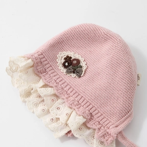 Pink knit baby girl bonnet with lace trim and bow accent on white background
