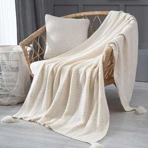 Nordic knitted cream white throw blanket with tassel detail on a wicker chair