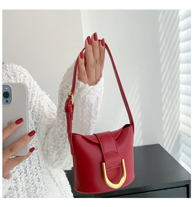 Detail showing red bucket bag with gold U-shaped hardware and adjustable shoulder strap