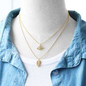 Detail of layered gold evil eye and leaf pendant necklace with zircon on a model
