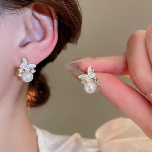 Close-up of butterfly pearl stud earrings with crystal inlays on a model's ear
