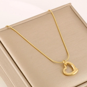 Detail of a gold heart pendant on a sleek snake chain over a textured jewelry box