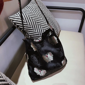 Close-up of black satin shoulder bag with white butterfly embroidery and pink beads