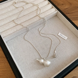 Dettaglio del ciondolo a zucca bianca su catena a serpente d'argento su lino beige