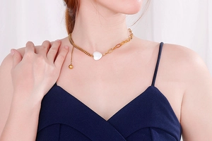 Detail of asymmetrical gold chain necklace with a white heart shell pendant on model