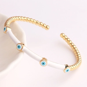 Detailed shot of gold plated evil eye cuff bracelet with white enamel on ceramic tray