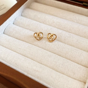 Detail of gold intertwined heart stud earrings on a white velvet jewelry box
