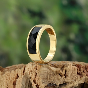 Close-up of golden stainless steel ring with rectangular black gemstone on wood base