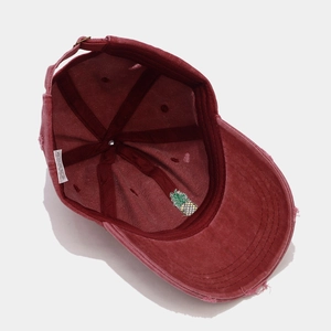 Detail of burgundy distressed baseball cap showing pineapple embroidery and inner lining