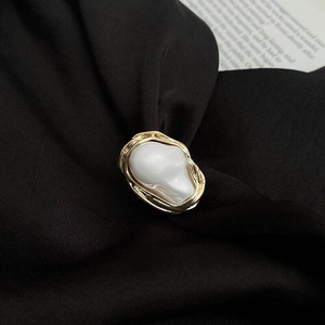 Macro detail of irregular baroque pearl ring with golden wire wrap on black silk fabric