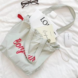 Flat lay of bean green canvas drawstring tote bag with red Bonjour text and daily gadgets