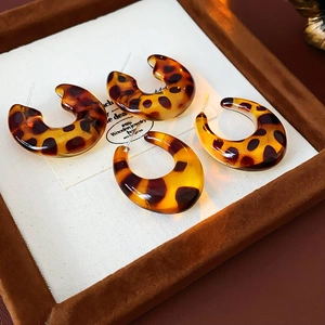 Detail view of two pairs of leopard print resin C-shaped hoop earrings on jewelry tray