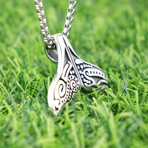 Polished silver whale tail necklace with tribal engravings on green grass background