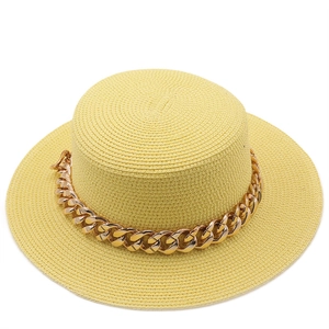 Detail view of woven yellow straw boater hat with a chunky gold metal chain decoration