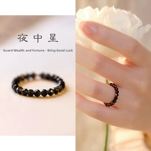 Close-up of a faceted black bead ring on a hand with elegant white floral accents