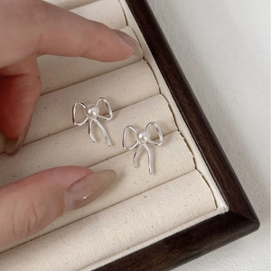 Close-up of a silver bow knot pearl stud earring held over a beige jewelry box