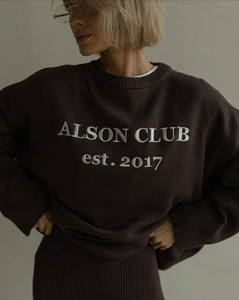 Detail of white embroidery text on a dark brown crewneck knit sweater with premium texture