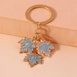 Close-up of golden keychain featuring three grey enamel maple leaf charms on stone