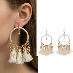 Detail view of Bohemian hoop earrings with white cotton fringe and gold beaded accents