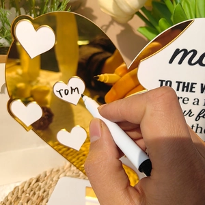 Close-up of hand writing names on small heart inserts for acrylic Mother's Day plaque