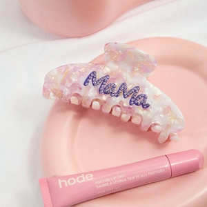 Pink marble acetate claw clip with purple rhinestones spelling Mama on a ceramic tray