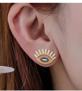 Detailed shot of a gold devil eye earring with blue and white crystals on ear