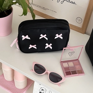 Detail of black makeup bag with pink bows and double zippers on a display shelf