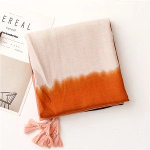 Detail of a beige and orange gradient scarf with pink tassels next to a minimalist book