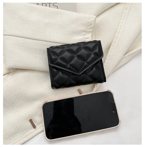 Compact black quilted wallet shown next to a smartphone to demonstrate the mini size