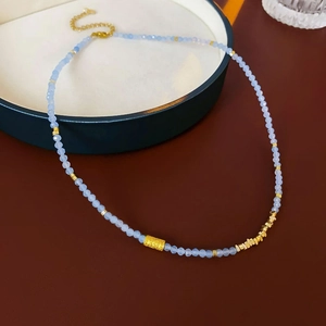 Détail d'un collier de perles bleu clair avec pendentif doré texturé sur un plateau