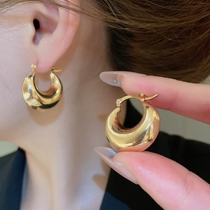 Close-up of chunky gold C-shaped hoop earrings with polished mirror finish on ears