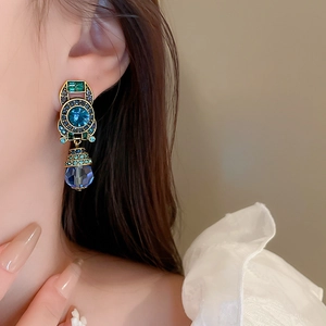 Close-up of vintage gold drop earrings with blue crystal worn by a model