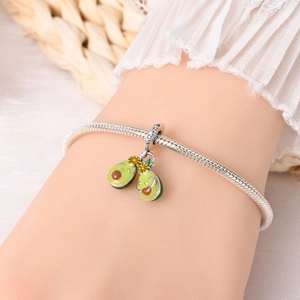 Close-up of silver snake chain bracelet featuring two cute green avocado charms on a wrist