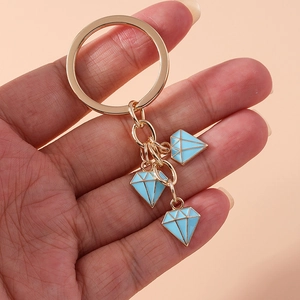 Close-up of hand holding a gold keychain with three light blue diamond-shaped enamel charms