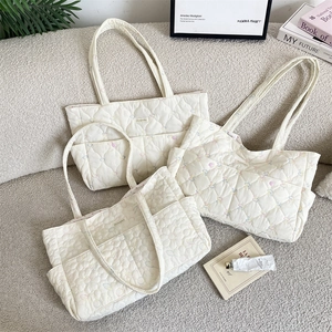 Three beige quilted tote bags with colorful heart and floral embroidery patterns
