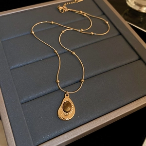 Detailed view of teardrop tiger eye pendant with gold chain in a gray jewelry box