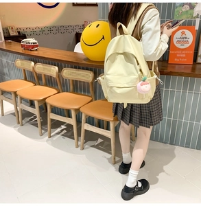Detail view of a pale yellow minimalist backpack with a pink plush charm for students