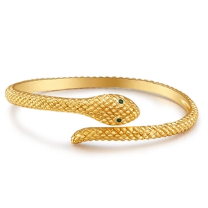 Macro detail of gold-plated snake bracelet with green stone eyes and scale texture