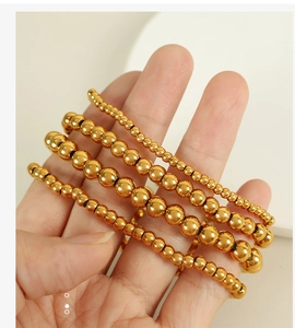 Detail showing five different sizes of golden stainless steel bead bracelets on a hand