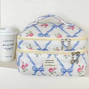 Détail d'une trousse à maquillage matelassée avec roses, nœuds bleus et zip fleuri