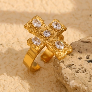 Macro shot of 18K gold plated cross ring with clear zircons on a textured stone base